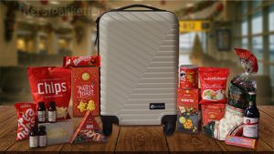 Luxe kerstpakket met taupekleurige trolley, rode kerstverpakking, snacks, chocolade, wijn en travelset op houten tafel