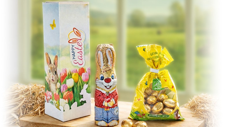 Happy Easter geschenkdoos met chocolade haas en Hamlet paaseitjes op houten plank in lentesfeer